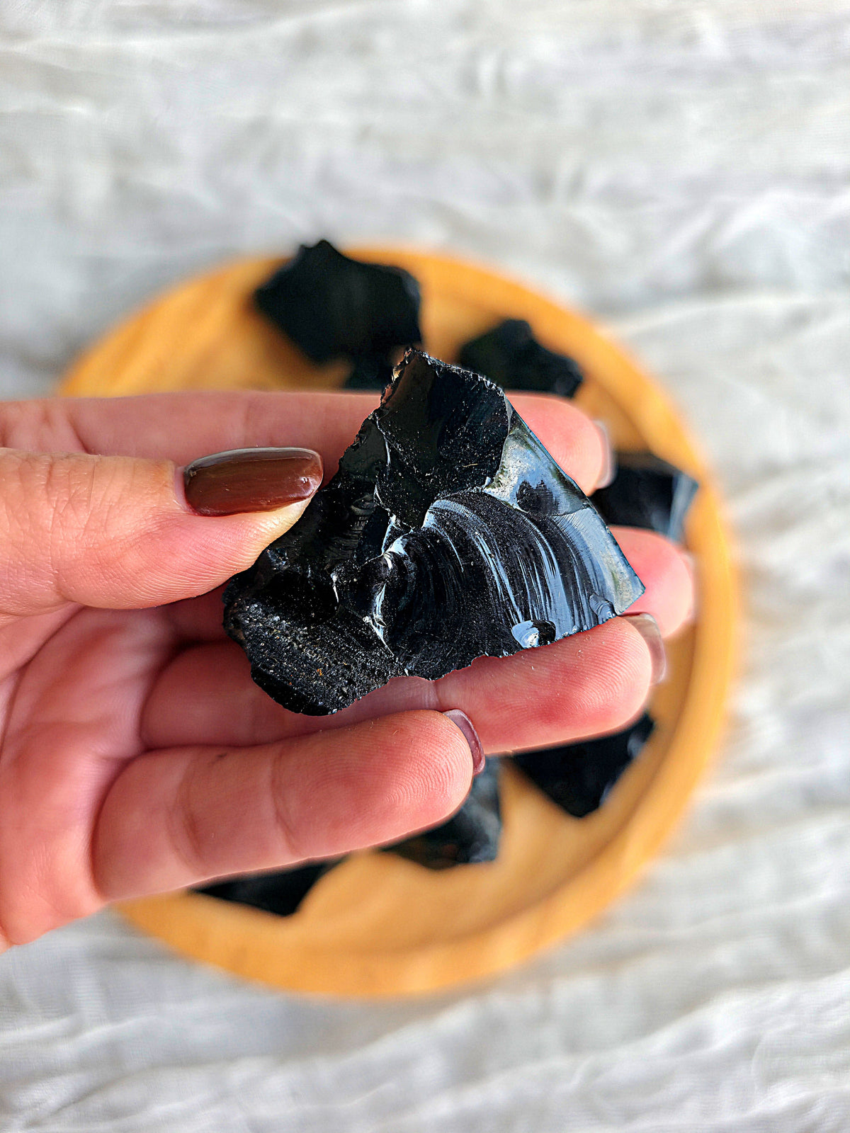 Obsidiana negra en bruto sostenida en la palma de la mano para apreciar su tamaño real.