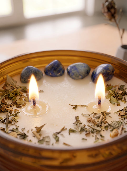 vela aromática artesanal Anamaya, decorada con rodados de sodalita y una sinergia de aromas de palo santo, vainilla, maderas, orégano, mirra, mandarina, rosas y bayas zoom encendida