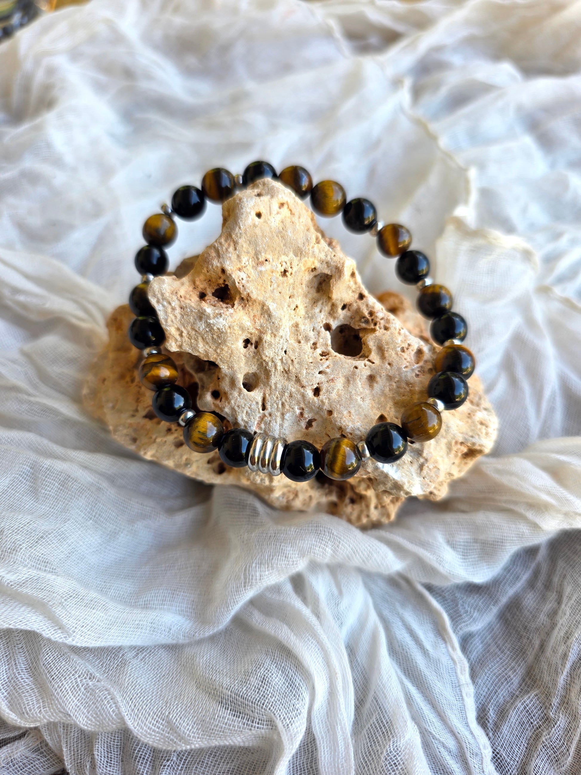 Detalle de pulsera plateada con perlas de ojo de tigre y ónix en acero inoxidable