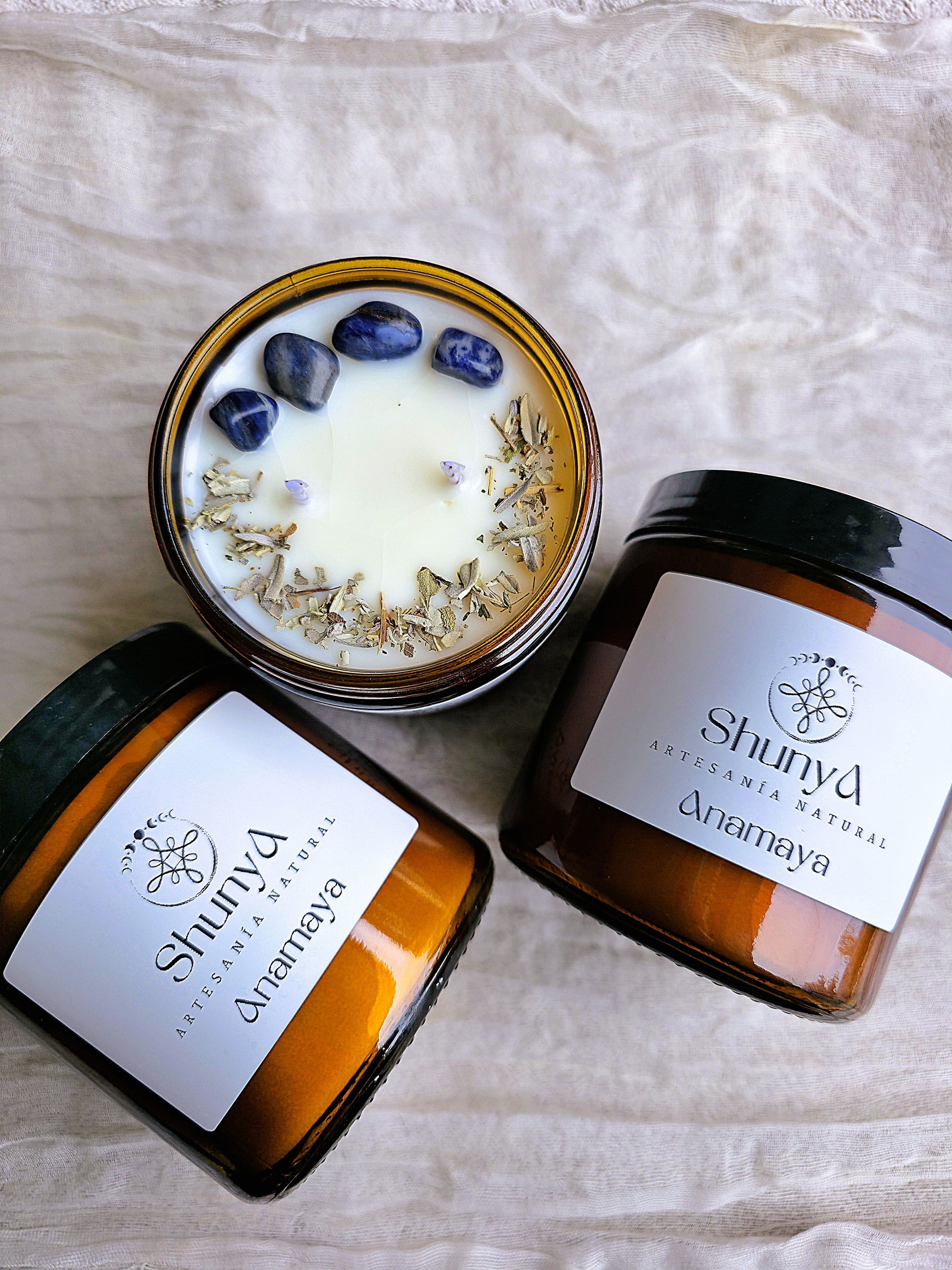 vela aromática artesanal Anamaya, decorada con rodados de sodalita y una sinergia de aromas de palo santo, vainilla, maderas, orégano, mirra, mandarina, rosas y bayas